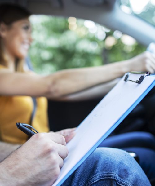 close-up-view-driving-instructor-holding-checklist-while-background-female-student-steering-driving-car